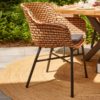 Delphine Coral and Provence table photo environment, On a terrace with a gray ceramic floor and on a round esparto rug, the chair is turned to show the wonderful cross legs of the table