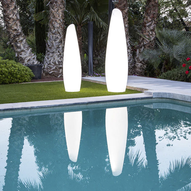 lámpara solar FREDO 140 y 160 de NewGarden® se ven sobre el césped detrás de una piscina