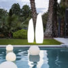 lámpara solar FREDO 140 y 160 de NewGarden® se ven sobre el césped detrás de una piscina donde hay 4 lámparas solares BULY flotando en el agua