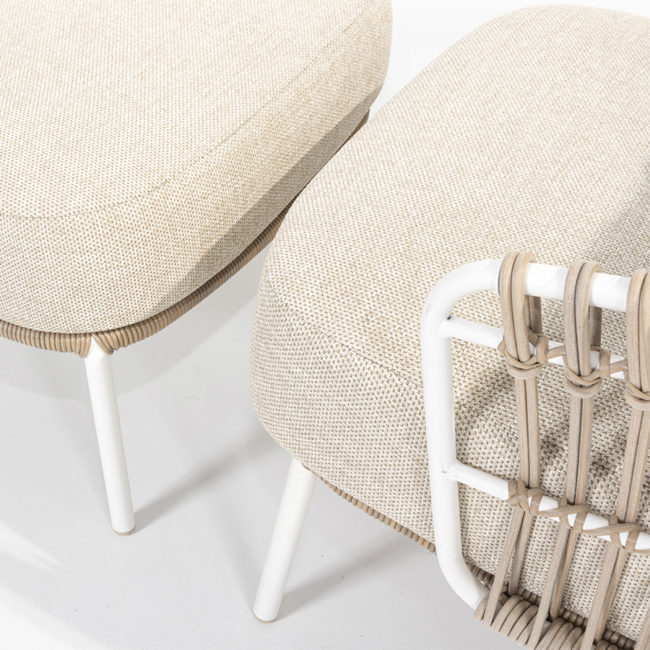 DALIAS armchair with footrest - 4 Seasons Outoor® with thick cushions that maximize the comfort of the seat and backrest, marbled in beige and tan beige. Armchair with footrest with tubular stainless steel structure in white, embellished with hand-woven hularo wicker around the structure in a toasted beige tone imitating traditional wicker. Detail of the armrest and the cushions of both the seat and the footrest.