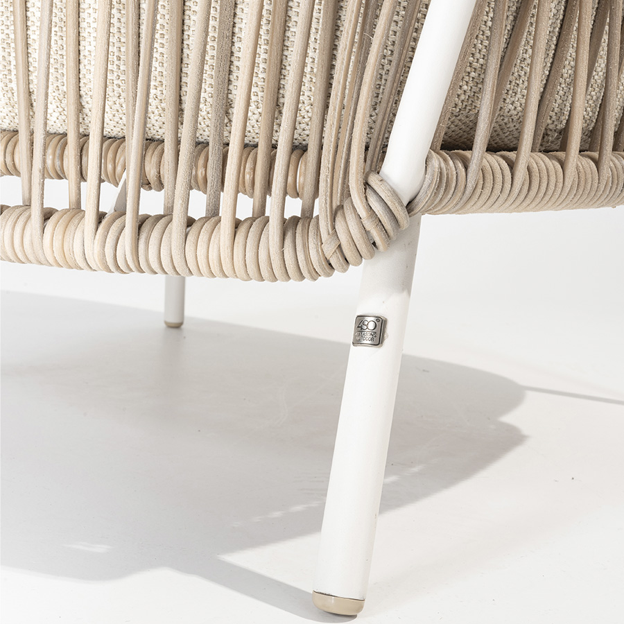 Detail of the wicker braiding on the lower structure of the 4 Seasons Outoor® DALIAS Armchair with thick cushions that maximize the comfort of the seat and backrest, marbled in beige and tan beige. Armchair with tubular stainless steel structure in white, embellished with hand-woven hularo wicker around the structure in a toasted beige tone imitating traditional wicker. Right side view on white background.