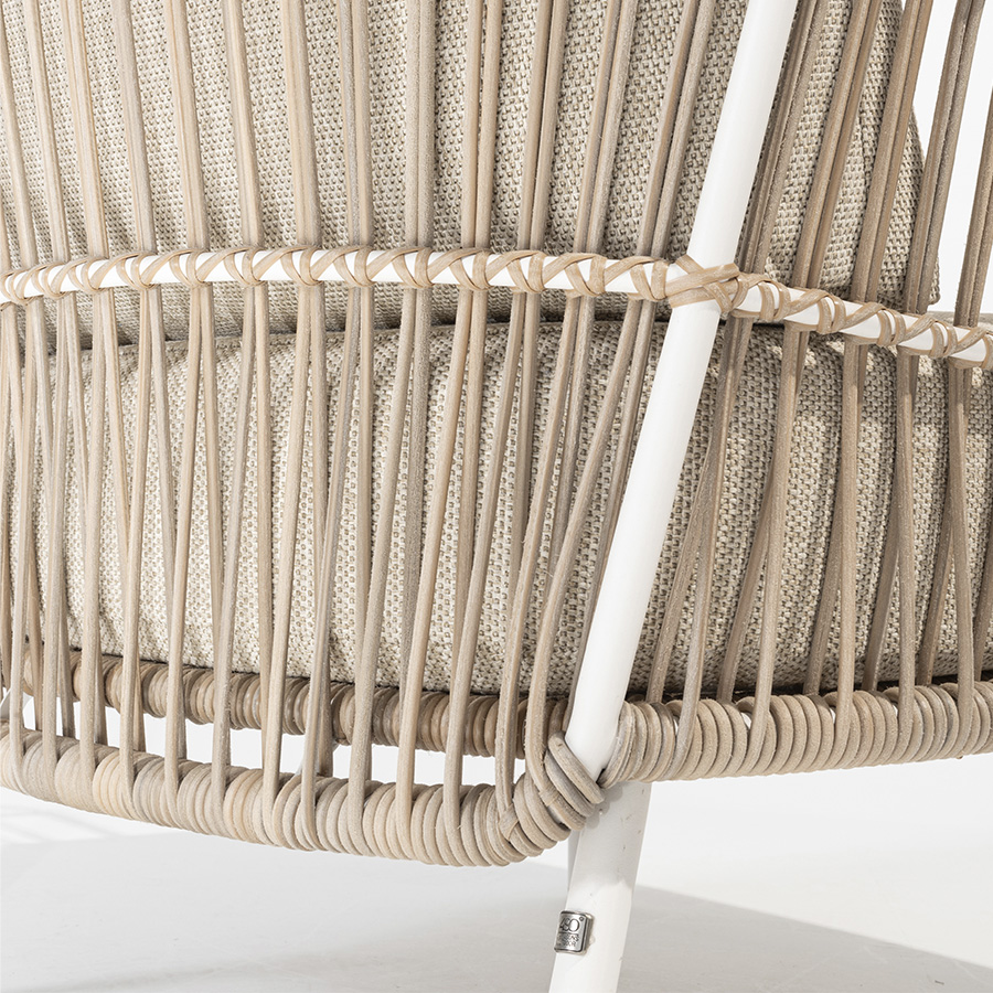 Detail of the wicker braiding on the structure of the 4 Seasons Outoor® DALIAS Armchair with thick cushions that maximize the comfort of the seat and backrest, marbled in beige and tan beige. Armchair with tubular stainless steel structure in white, embellished with hand-woven hularo wicker around the structure in a toasted beige tone imitating traditional wicker. Right side view on white background.