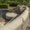 The Sardinia garden sofa by 4SO is a curved sofa with a chaise longue, seating 4. Its curved stainless steel frame is finished in a beautiful tan beige, a rich, toasted shade of café au lait. Rope in the same tones creates a triangular pattern that allows for airflow and adds a touch of sophistication. The generous cushions ensure exceptional comfort. Angled view of the backrest with the chaise longue in the background. Lifestyle photo on a wooden decked terrace surrounded by lush green hedges.