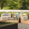 Sofá jardín Vanessa de Hartman, un sofá en dos módulos que forman un precioso sofá curvo que recuerda a los de mediados de siglo. Tapizado con tejido Sunbrella el más resistente del mercado en un tono gris perla muy elegante. Delante aparece el set de mesas carson en negro. Foto ambiente.