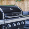 The Fireside Sahara A450 gas barbecue features an enameled cast iron grill that seals in flavours and 4 stainless steel burners plus a side burner. A thermostat in the lid allows you to regulate and monitor the temperature while grilling. This barbecue is a worthwhile investment in quality. It has an integrated and easy-to-use electric ignition system. It features a concealed compartment for the gas cylinder. A wooden cutting board extends from the right side shelf. The knobs and handles are silver, while the rest is black. An elegant combination that never fails. Oblique detail view of the lid, shelves and knobs.