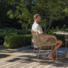 Comedor Prado Barrel Murcia de 4SO plano frontal de la silla Murcia con un hombre joven sentado a la mesa Prado Barrel en una terraza de madera y al fondo un jardín. Cómpralo en De Tropen, tu experto en muebles de jardín y terraza.
