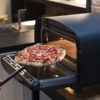 URBE electric oven by Alfa Forni. A pizza is being taken out of the oven with the peel. Find it at De Tropen, official Alfa Forni supplier in Spain and Portugal.