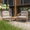 Conjunto Sillones de teca Nora de 4SO Se ve el conjunto de sillones hechos de teca con una forma ergonómica y redondeada que se embellecen con la cuerda en color topo anudada a la estructura desde los reposabrazos hasta la base del asiento rodeando todo el sillón y creando un patrón característico de la colección Nora. Tanto las patas como la estructura es cilíndrica y suave. Incluye tanto el cojín de asiento como el del respaldo en diferentes tonos de beige tostado. Cómpralo en De Tropen, tu experto en muebles de jardín y terraza. Foto ambiente del conjunto de sillones Nora (2 sillones) con la mesa Finn en medio, colocados en una terraza de azulejos y delante de una moderna casa de madera y barandilla metálica. Delante a la izquierda puedes ver la hierba y por detrás unas preciosas hortensias blancas que sobresalen por el muro lateral.