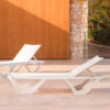 Se ven 2 Tumbonas Voxel en Blancas de Vondom, en una terraza de suelo porcelánico en color beige arena, con un muro de madera y piedra al fondo. Diseñada por Karim Rashid Encuéntrala en la mayor tienda de muebles de exterior, De Tropen.