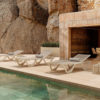 Se ven 3 Tumbonas Voxel de Vondom en Ecru al borde de una piscina por detrás una pared de piedra natural a la izquierda y a la derecha una sala con un comedor. La tumbona está diseñada por Karim Rashid. Encuéntrala en la mayor tienda de muebles de exterior, De Tropen.