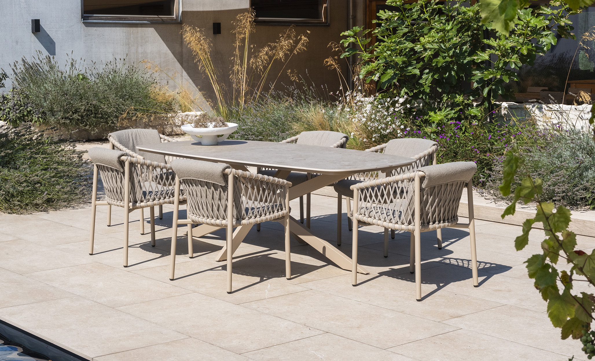 Comedor Prado Barrel - Allora Latte de 4SO Mesa Prado con estructura de acero inoxidable terminada con pintura en polvo de color latte, un tono beige tostado o café con leche y tablero cerámico. Las sillas Allora de aluminio y cuerda en latte. Cómpralo en De Tropen, tu experto en muebles de jardín y terraza.