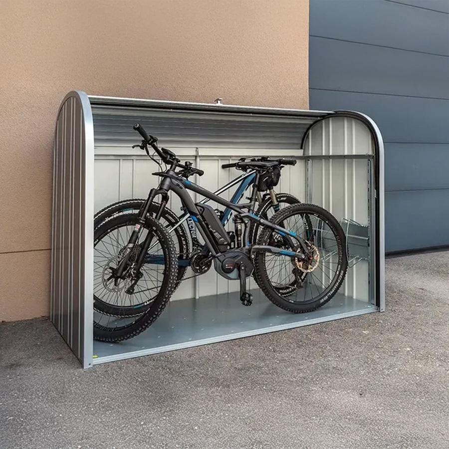 Arcón StoreMax Plata de Biohort. Foto ambiente, se ve el baúl de jardín colocado contra una pared, junto a la entrada del garaje. El arcón está abierto y se ven dos bicicletas dentro. Encuéntralo en De Tropen al mejor precio. Confía en la mayor tienda de muebles de exterior de Málaga.