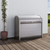 Arcón StoreMax Gris cuarzo de Biohort. Foto ambiente, se ve el baúl de jardín colocado en una terraza con una planta a la izquierda y pegado a una pared blanca. Encuéntralo en De Tropen al mejor precio. Confía en la mayor tienda de muebles de exterior de Málaga.