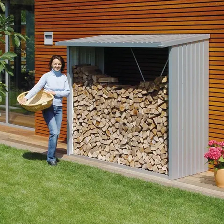 Leñero Woostock 230 de Biohort. Foto ambiente se ve una mujer con un canasto junto al leñero en plata, que está casi lleno de leña. Encuéntralo en De Tropen, la mayor tienda de muebles de jardín de Málaga.