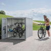 Biohort Mini Garage. Photo of an open garage setting with two bicycles and a cyclist on the right. Find it at De Tropen for the best price. Trust the largest outdoor furniture store in Malaga.