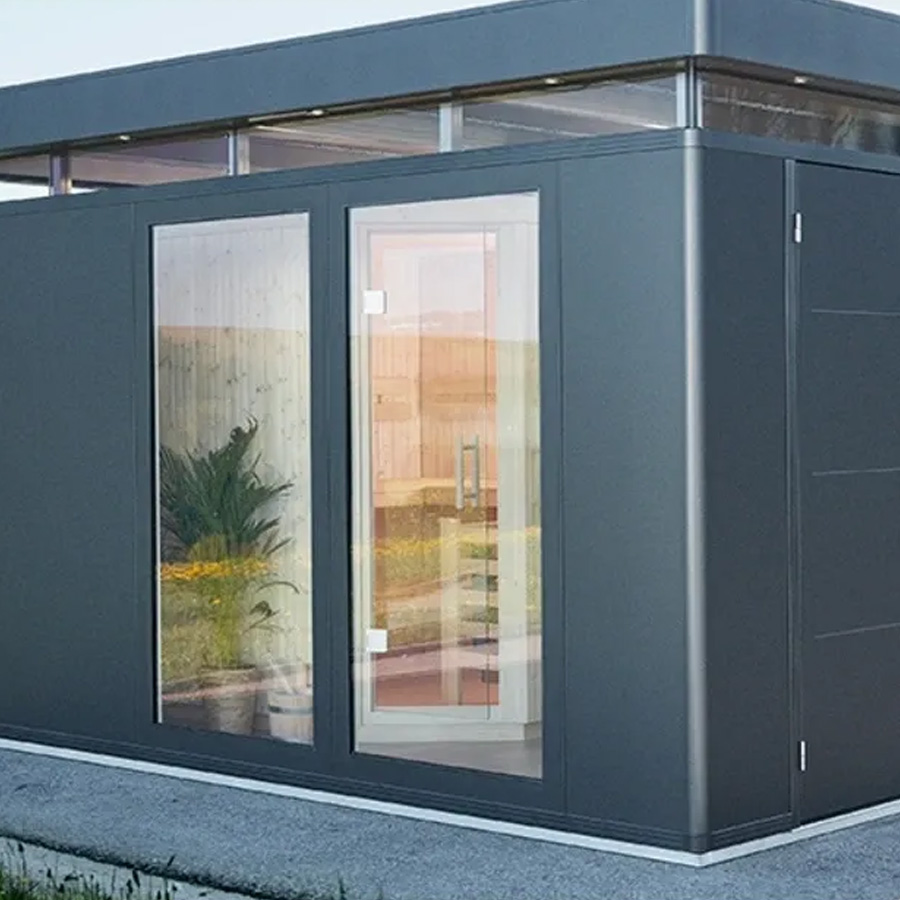 Foto ambiente Caseta CasaNova en gris oscuro de Biohort, se ve la sauna a través de los elementos de cristal instalados en el lateral. Amplía tus horizontes con De Tropen®, ven a descubrir las posibilidades de personalización de la CasaNova. En la mayor tienda de muebles de jardín de la Costa del Sol.