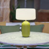 Phoebe 40 solar table lamp in green by NewGarden, lifestyle photo, the lamp lit on a white ceramic-top table. Expand your horizons with De Tropen®, come and discover the possibilities of lighting for your terrace or balcony. In the largest garden furniture store on the Costa del Sol, Málaga and Granada.