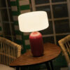 Phoebe 40 solar table lamp in burgundy by NewGarden, lifestyle photo, the lamp lit on a dark wood table. Expand your horizons with De Tropen®, come and discover the possibilities of lighting for your terrace or balcony. In the largest garden furniture store on the Costa del Sol, Málaga and Granada.